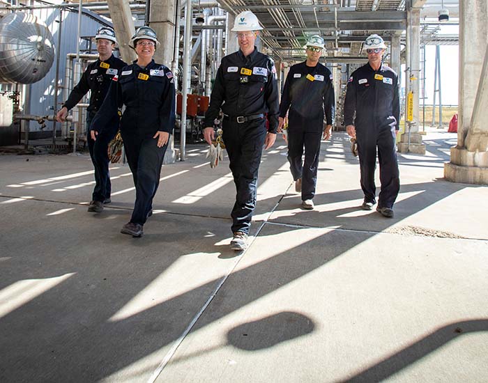 Team of five yd7610 employees walking through the Three Rivers refinery, surrounded by equipment.